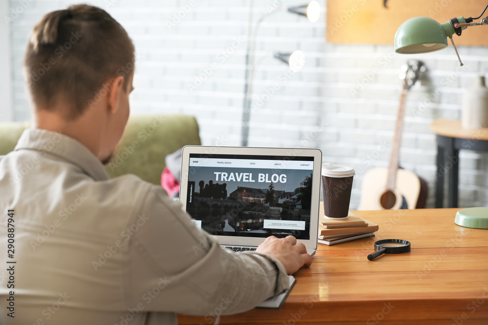 Male travel blogger with laptop at table