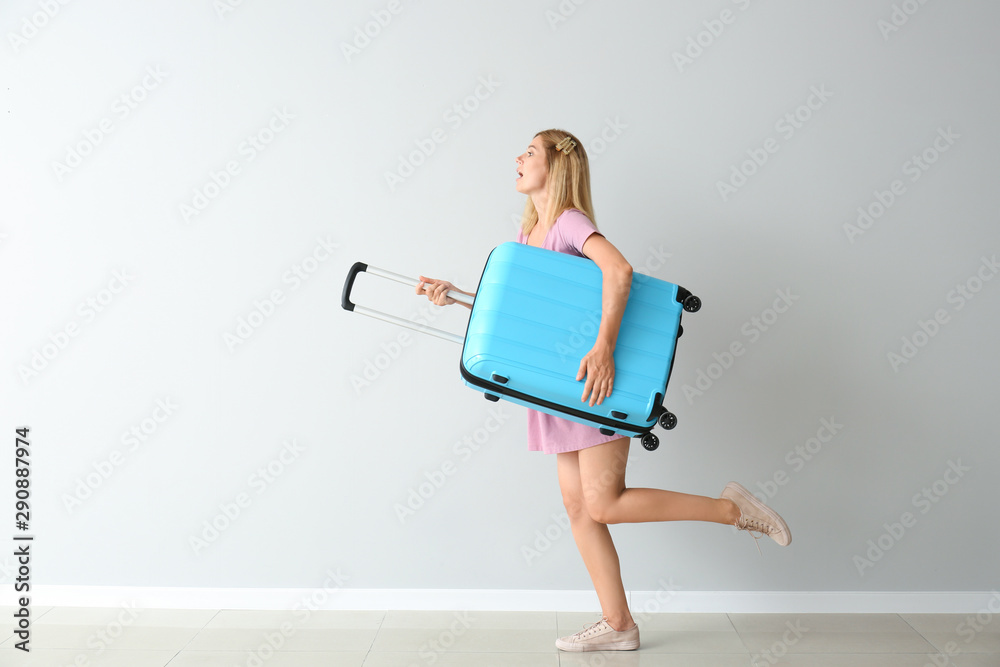 Running beautiful woman with luggage near light wall