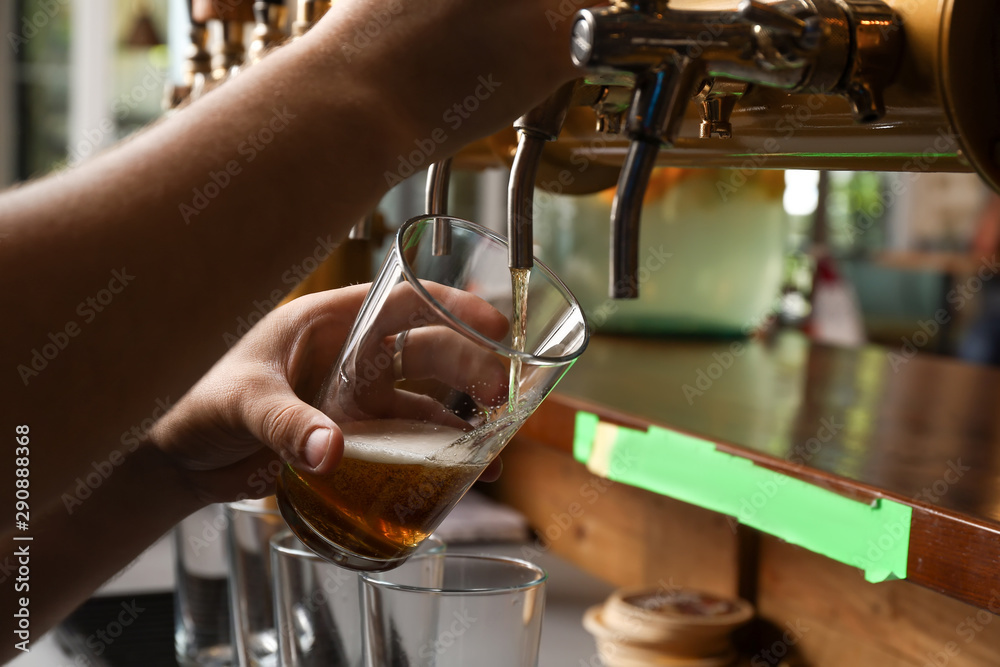 Barman pouring fresh beer in glass, closeup