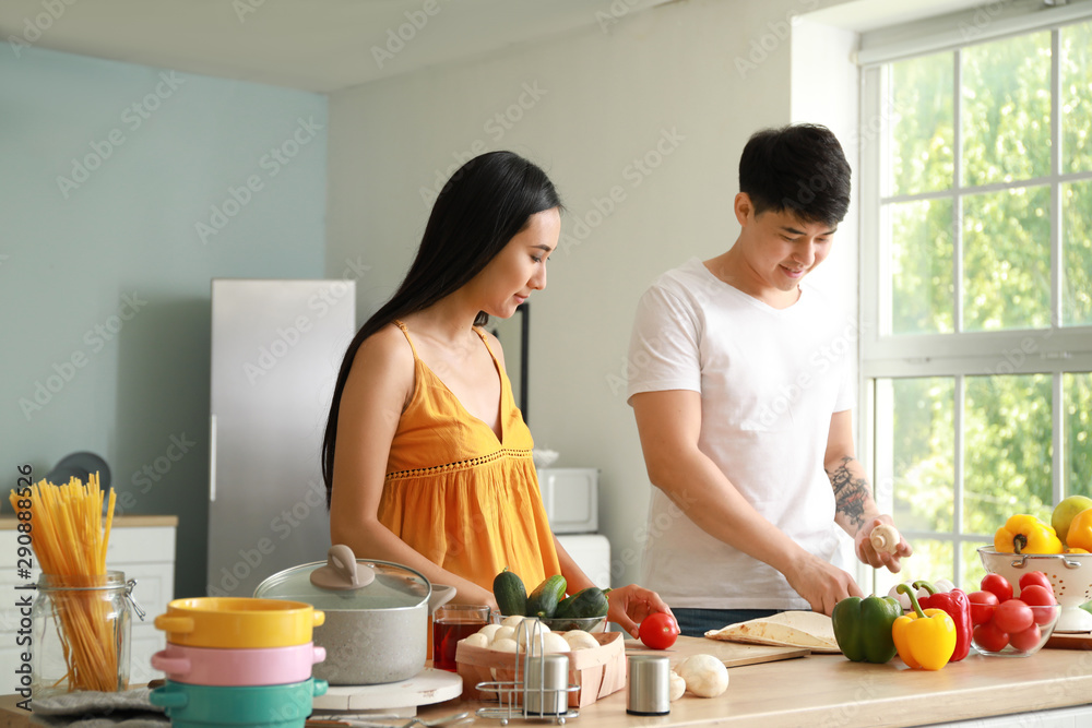 Happy Asian couple cooking together in kitchen