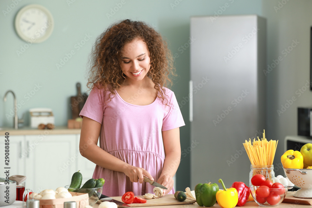 Beautiful African-American woman cooking in kitchen