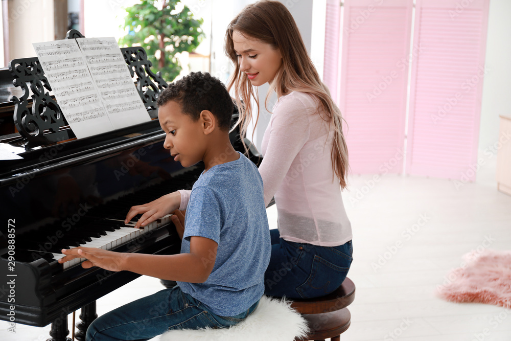 Woman teaching little African-American boy to play piano at home