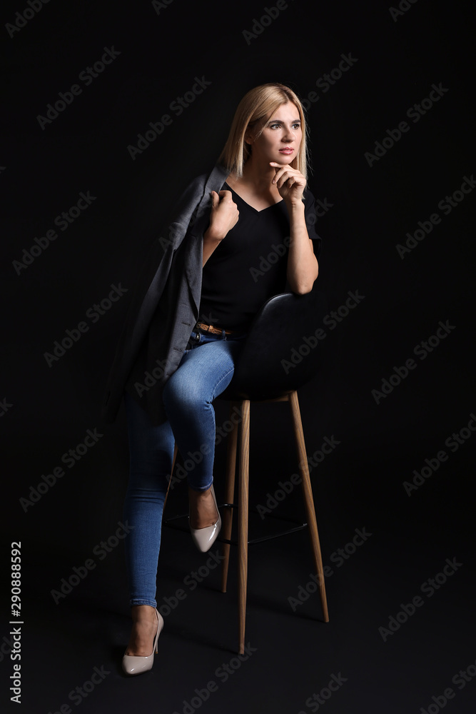 Beautiful stylish woman sitting on chair against dark background