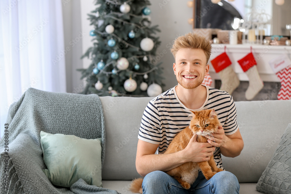 Young man with cute cat at home on Christmas eve