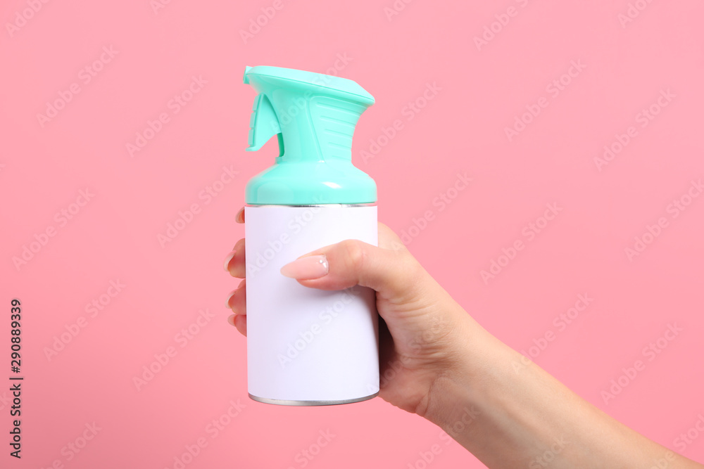 Female hand with bottle of air freshener on color background