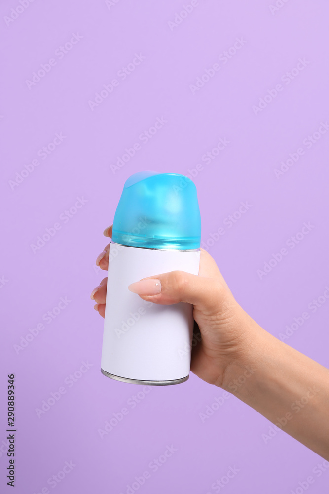 Female hand with bottle of air freshener on color background