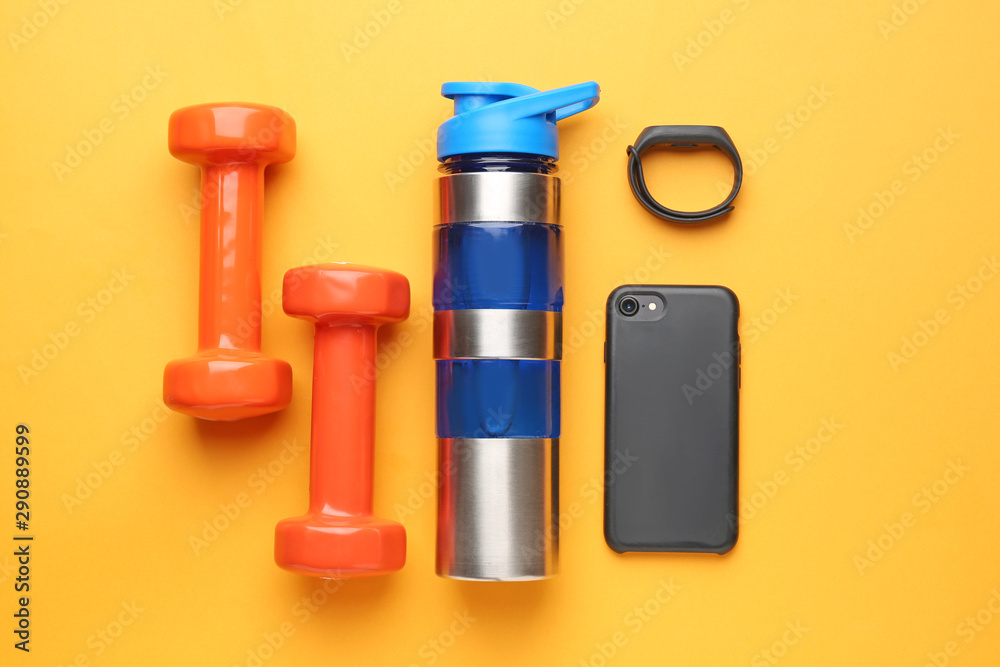 Sports water bottle, dumbbells, mobile phone and fitness tracker on color background