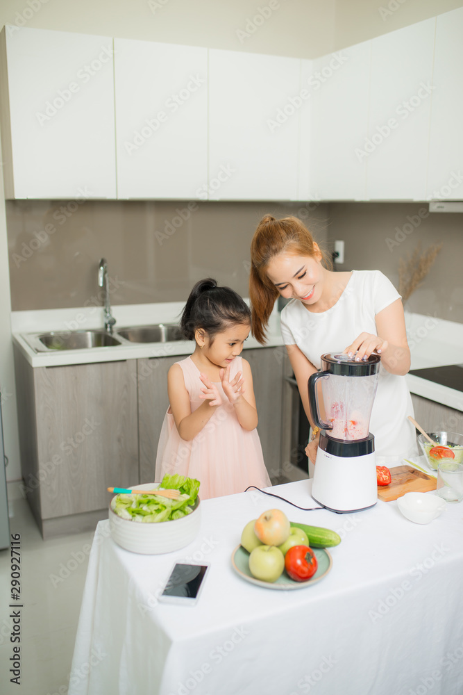 年轻的亚洲母亲和女儿正在制作新鲜挤压的番茄奶昔，女儿很开心