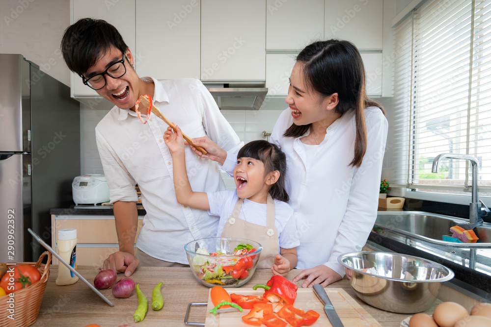 当一家人在工具包里做饭时，亚洲女儿正在给父亲和母亲喂沙拉