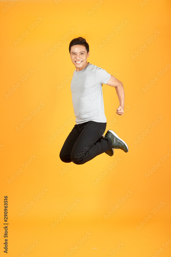 Full length portrait of an excited Asian man jumping over orange background