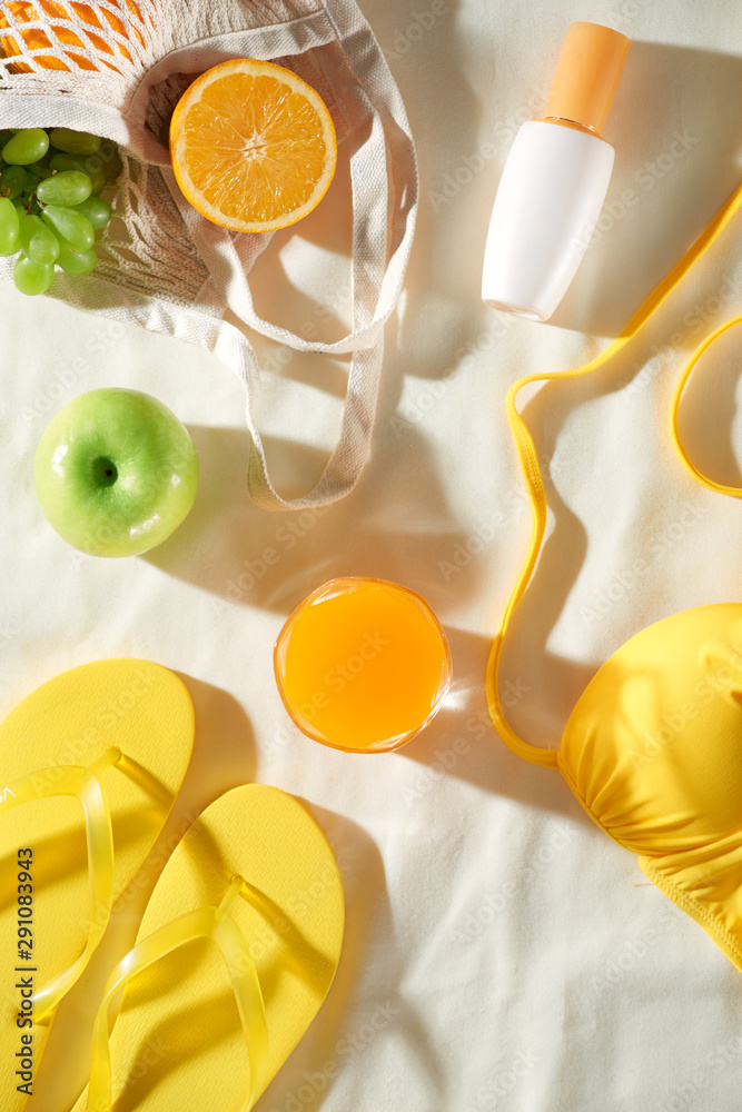 Summertime picnic on white background with fruit bag, flip-flop, sin cream and juice, flat lay