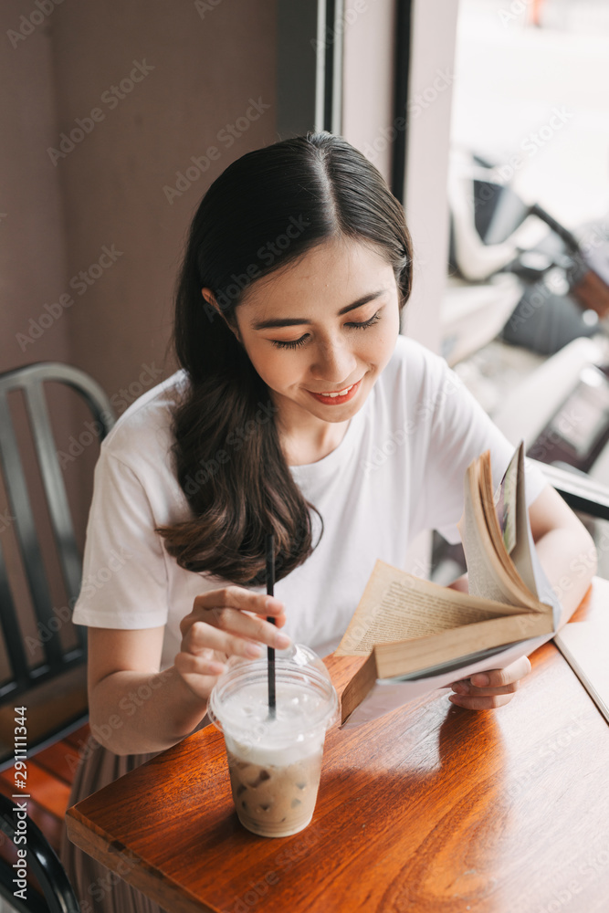 Picture of young pretty woman sitting at the table in cafe and reading book.