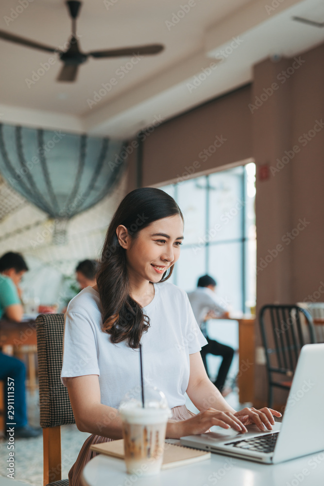 一位年轻迷人的商务女性坐在咖啡馆里，手里拿着笔记本电脑和咖啡