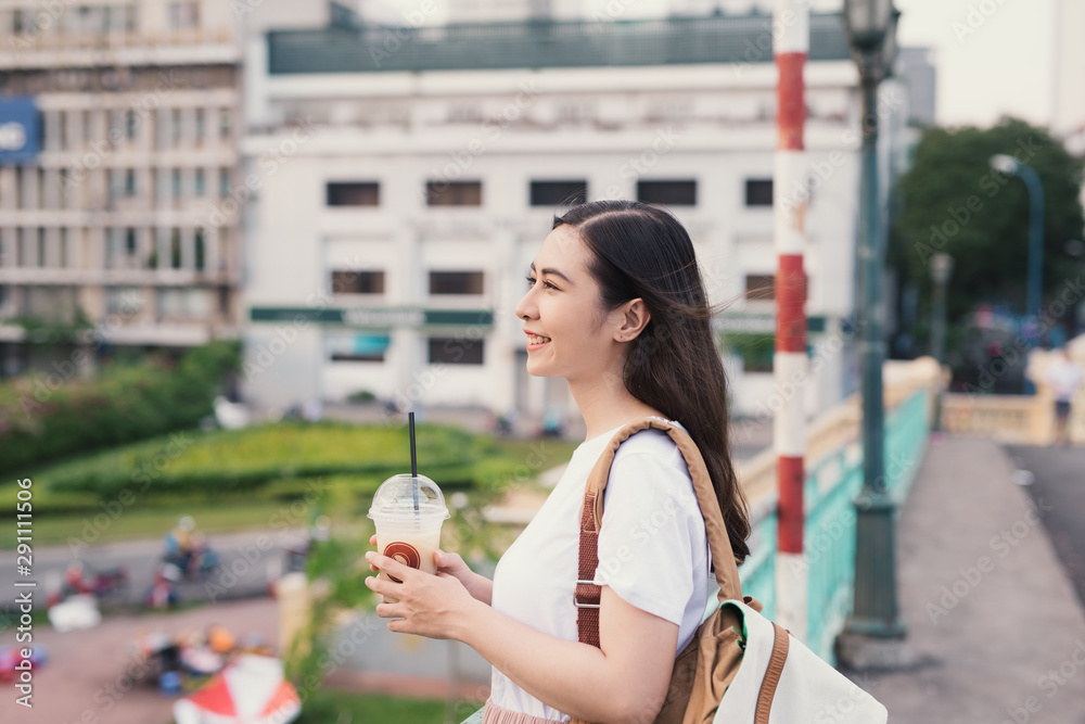 年轻可爱的女人在城市背景的桥上喝咖啡