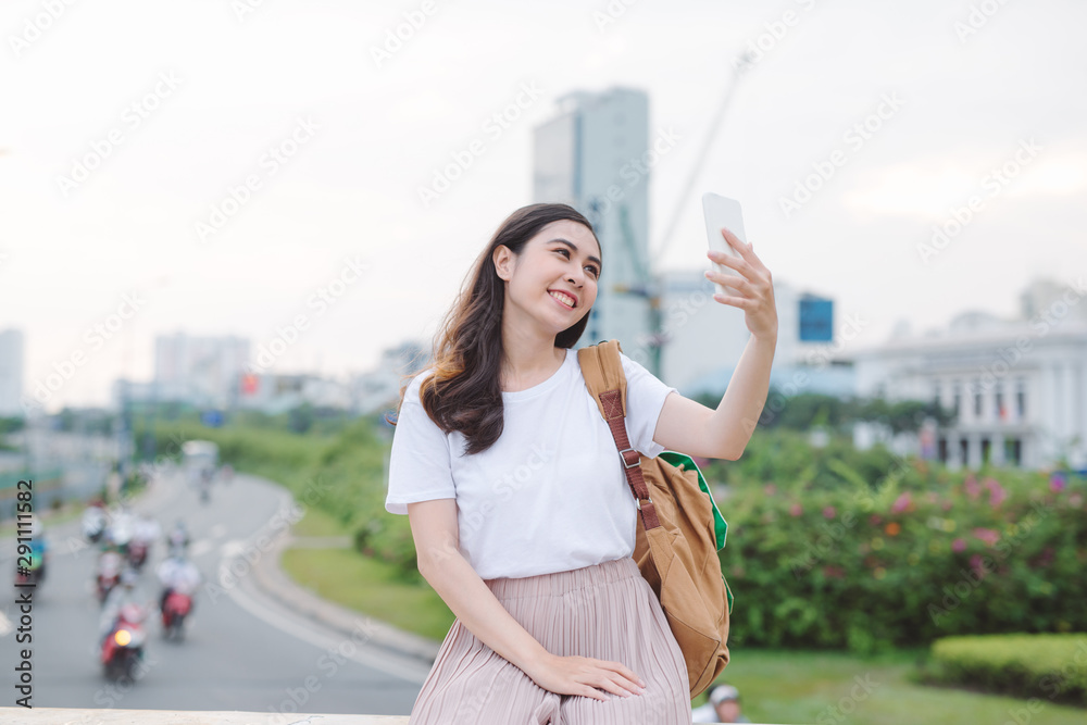 年轻女旅行者坐在市中心的桥上用手机自拍