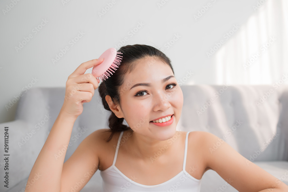 Portrait of beautiful young woman combing her hair, looking at camera and smiling