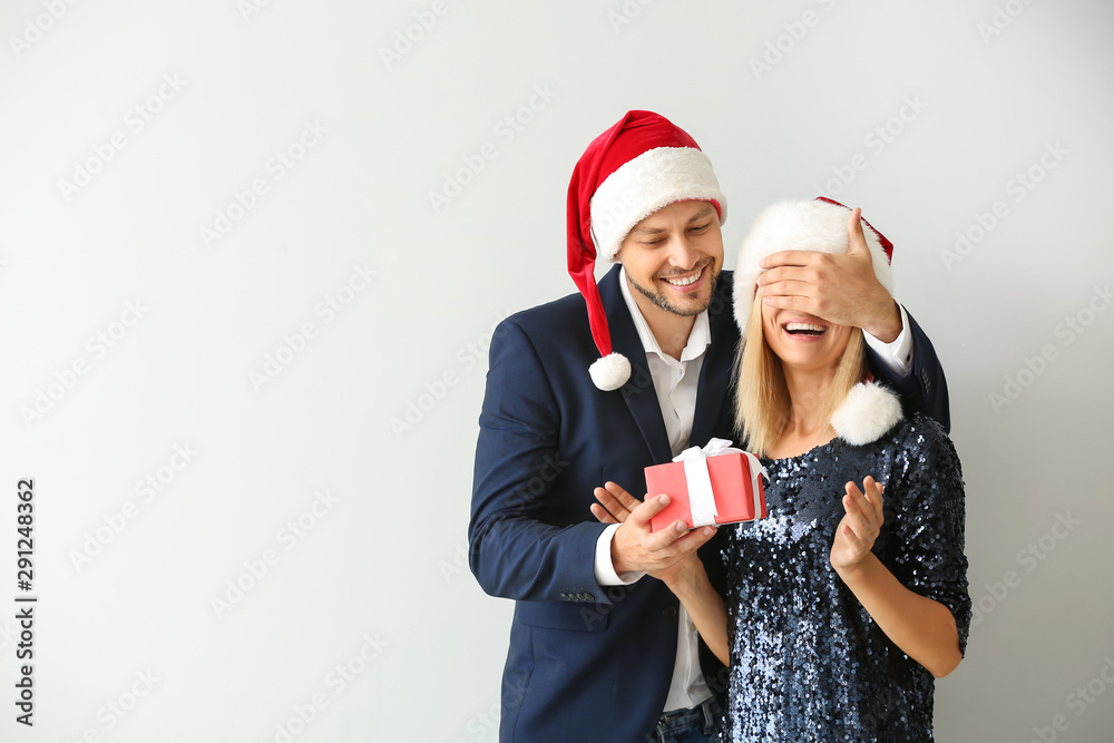 Man giving his wife Christmas present on light background