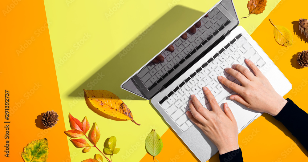 Person using a laptop computer with autumn leaves - overhead view