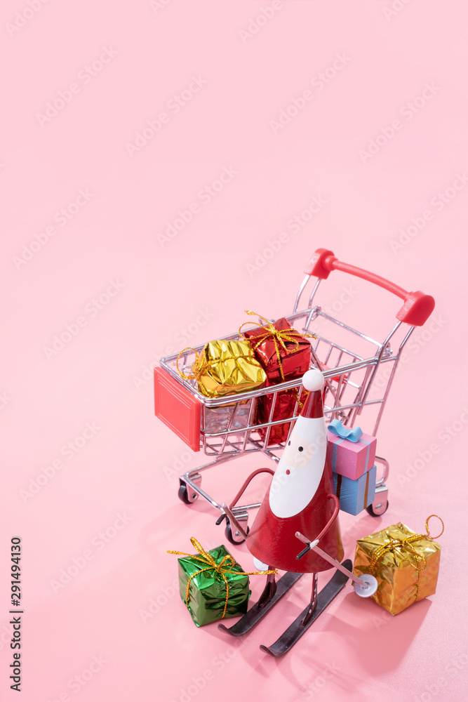 Christmas shopping concept, mini red shop cart trolley with Santa Claus toy and gift box isolated on