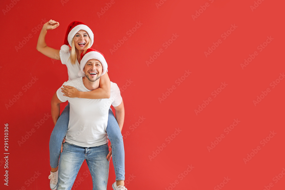 Happy couple in Santa hats on color background