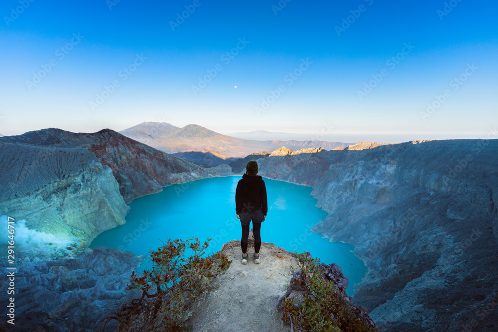 日出时，女孩站在Kawah Ijen火山口下的岩石上。看看世界上最大的酸湖。