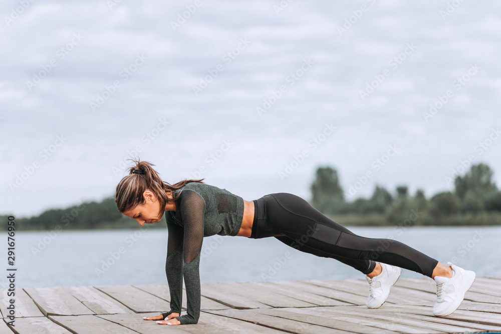 Side view of fit woman exercising on wooden river boardwalk.