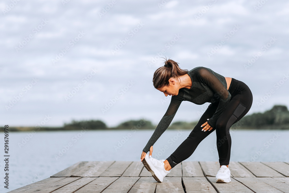 Young woman doing stretch exercise on a river bank.