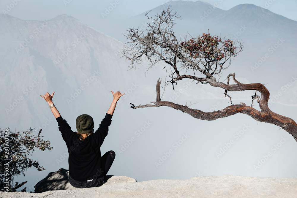 快乐的年轻女子坐在Kawah Ijen火山口上方的岩石上。看看世界上最大的酸湖。