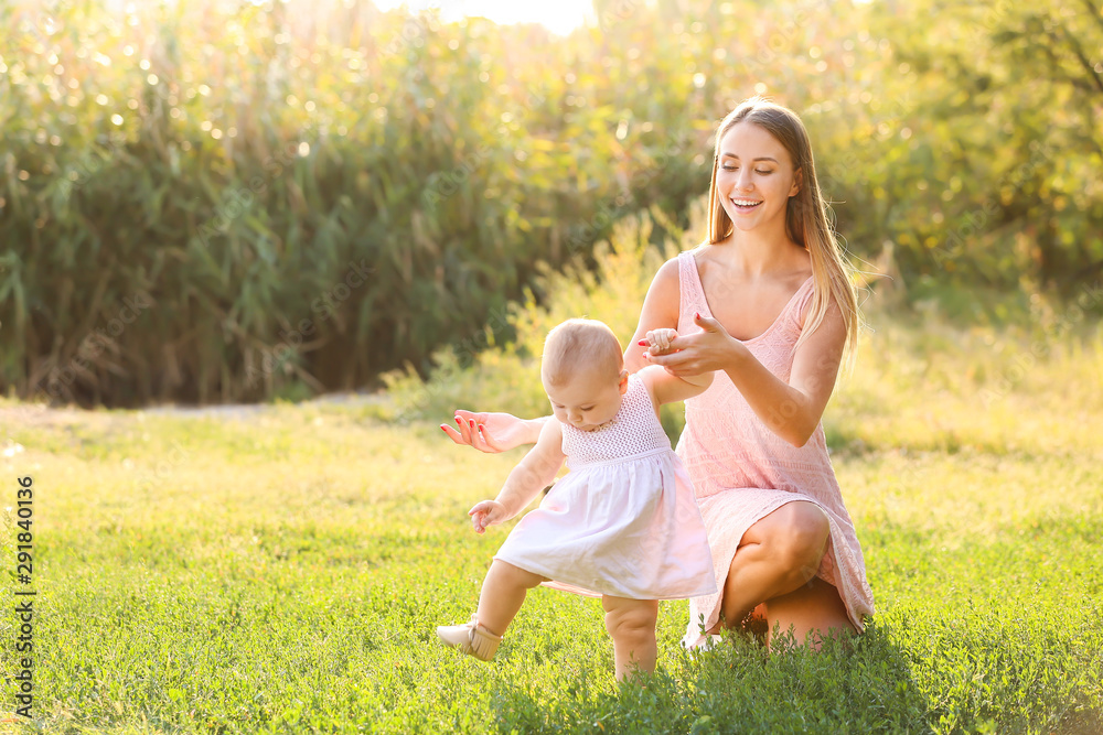 Mother teaching her little baby to walk outdoors