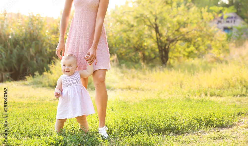 Mother teaching her little baby to walk outdoors