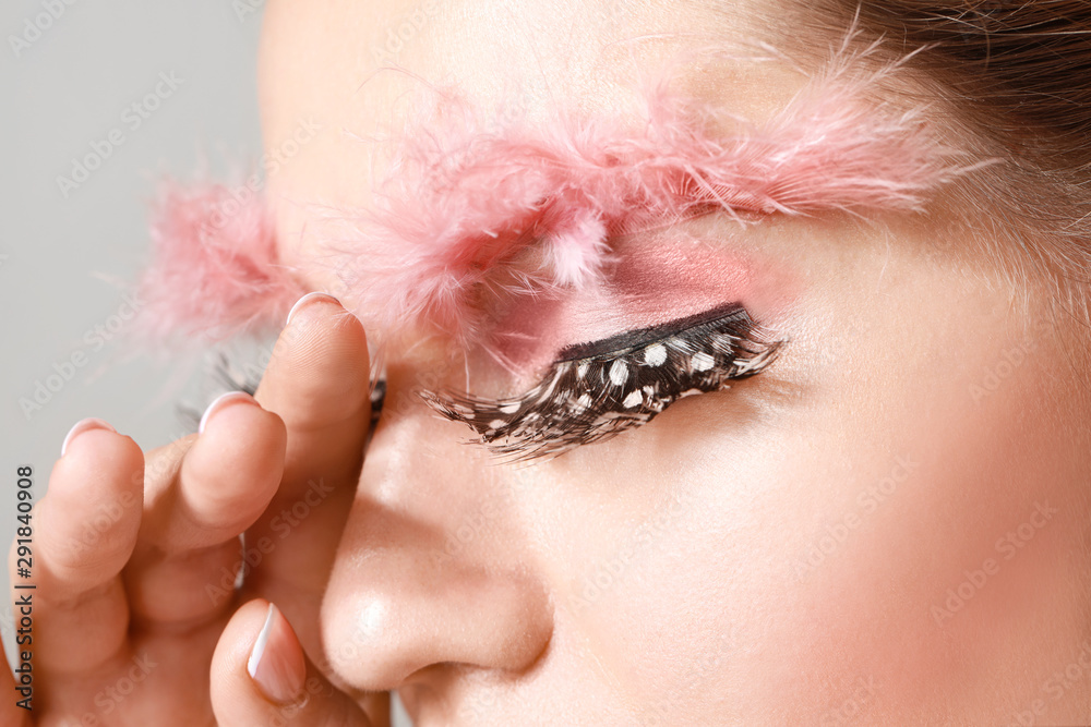 Young woman with creative eyelashes and eyebrows on grey background, closeup