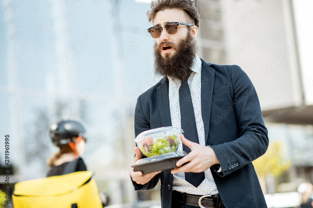 优雅的大胡子上班族在办公楼附近拿着快递员送来的外卖午餐