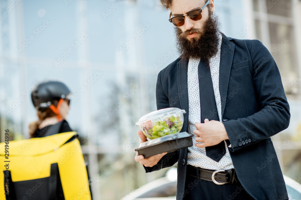 Elegant bearded office worker carrying takeaway lunch received from a courier near the office buildi