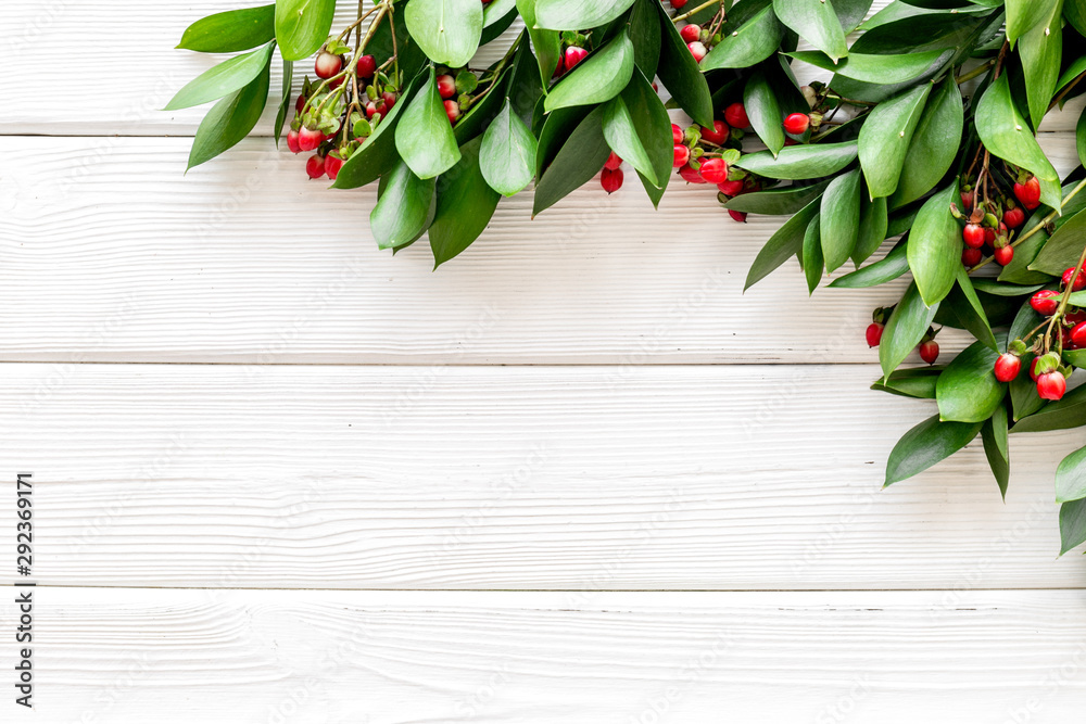 Green leaves and red berries frame on white wooden background top view copyspace