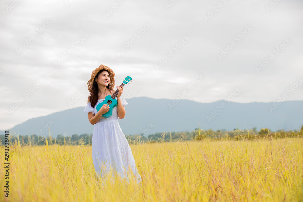 快乐肖像亚洲女人在秋天的草地上弹尤克里里吉他，生活方式健康