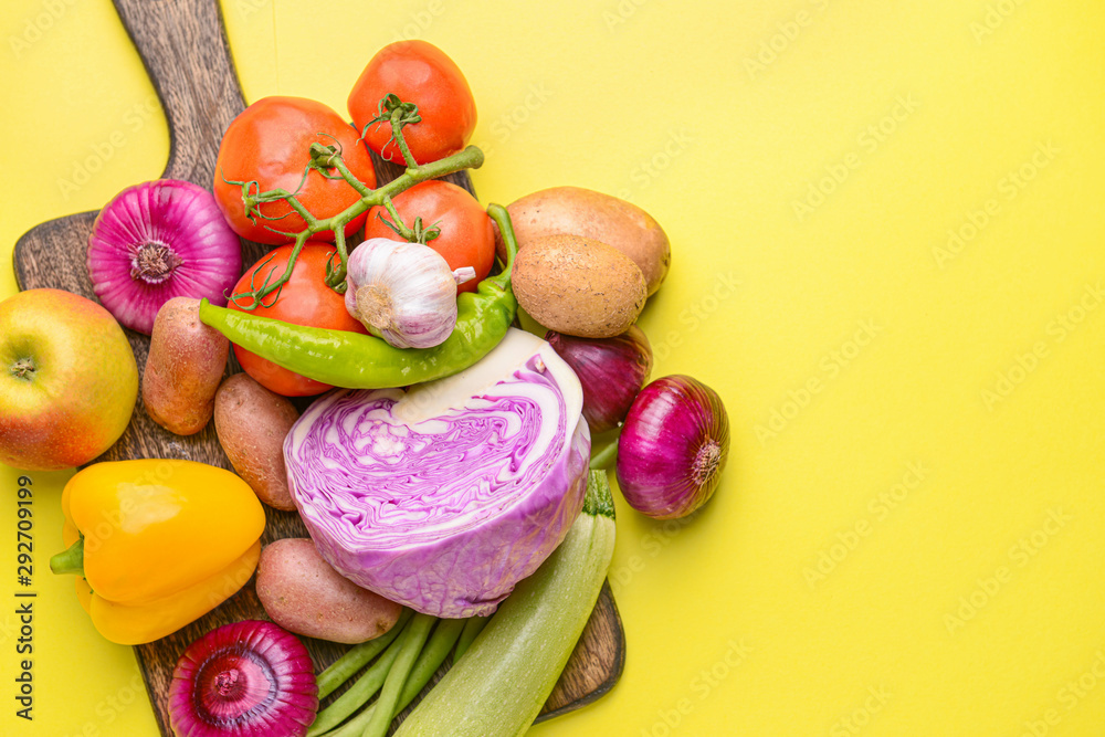 Board with many healthy vegetables on color background