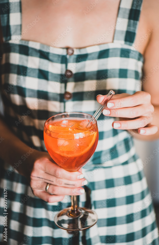 一位身穿格子连衣裙的年轻女士，手里拿着一杯Aperol雪碧开胃酒鸡尾酒，里面有橙子