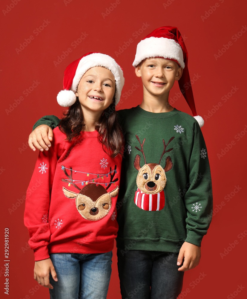 Cute children in Christmas sweaters and Santa hats on color background