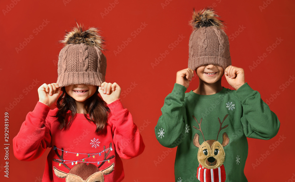 Cute children in Christmas sweaters and hats on color background