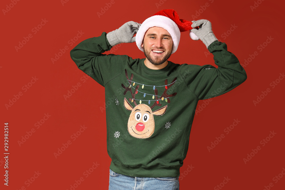 Young man in Christmas sweater and Santa hat on color background