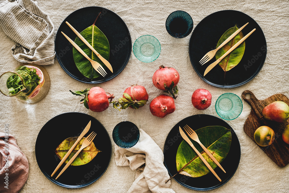 Autumn table styling for holiday dinner. Flat-lay of dinnerware with fresh fruits and fallen leaves 