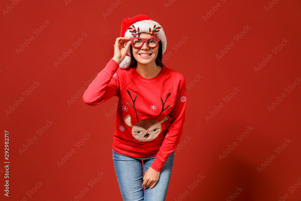 Funny woman in Christmas sweater and Santa hat on color background