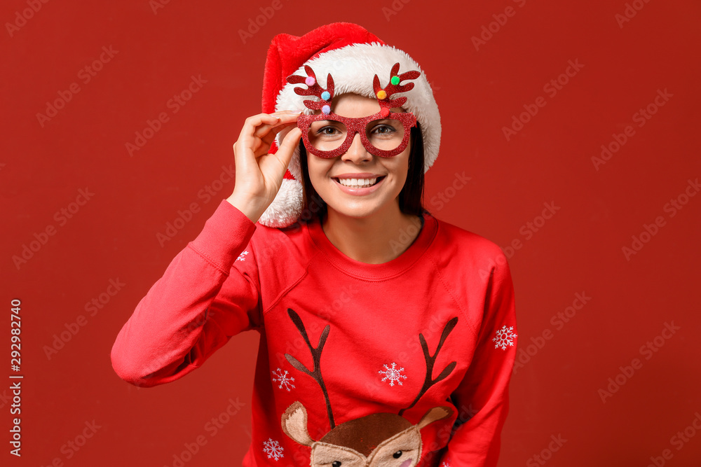 Funny woman in Christmas sweater and Santa hat on color background