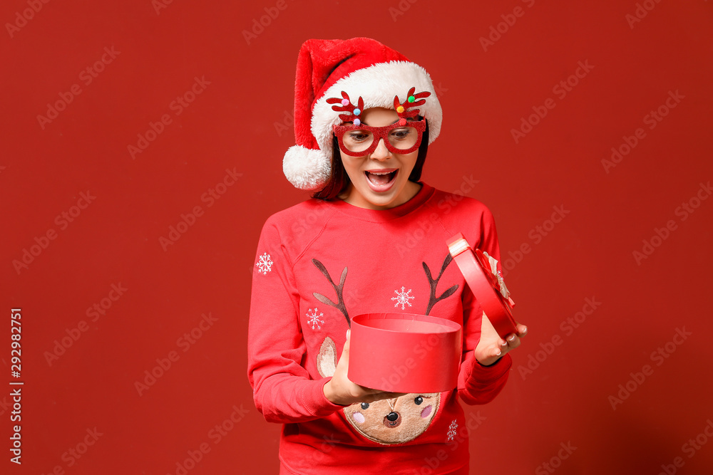 Funny woman in Christmas sweater and with gift on color background