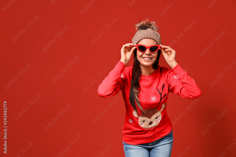 Young woman in Christmas sweater and knitted hat on color background