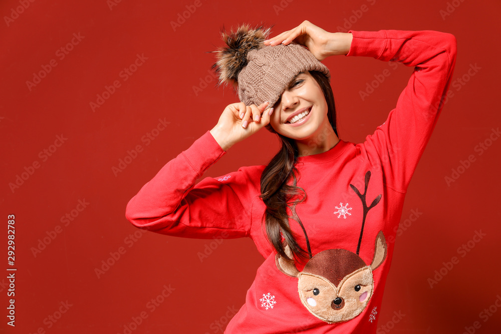 Young woman in Christmas sweater and knitted hat on color background