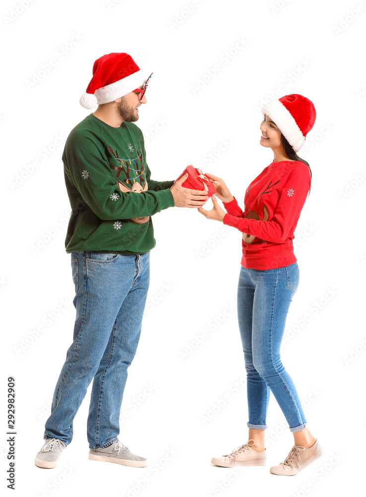 Young couple in Christmas sweaters and with gift on white background