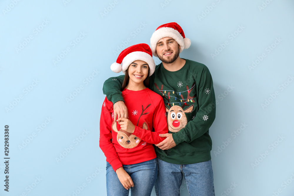 Happy couple in Christmas sweaters and Santa hats on color background