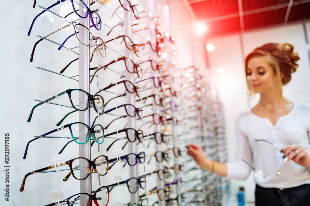 Beautiful young woman choosing new pair of spectacles in opticians store. Eyesight correction. Optic