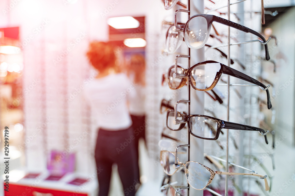 Eyeglasses shop. Stand with glasses in the store of optics. Woman trying on glasses in optical store